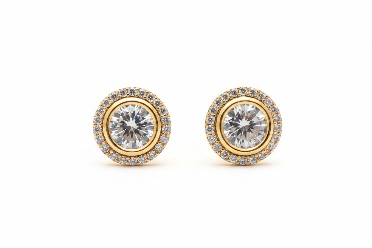 Gold earrings with clear gemstones on a beige background