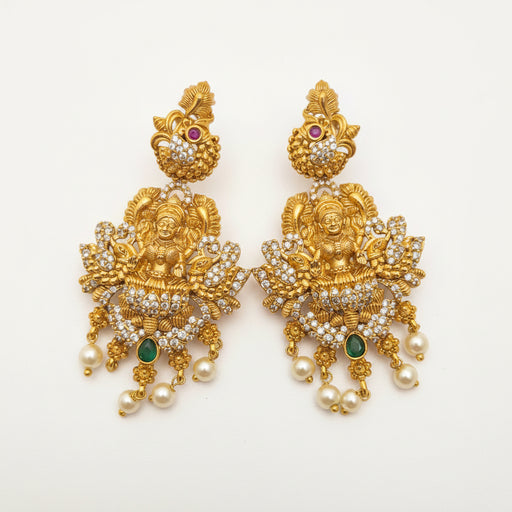 Pair of ornate gold earrings with pearls and gemstones on a beige background