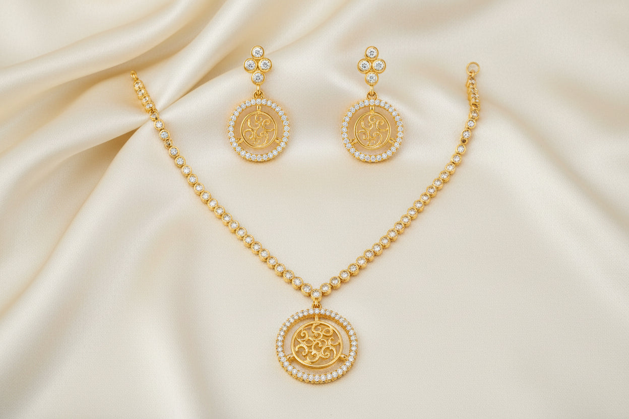 Gold-tone necklace and matching drop earrings set with circular Om symbols surrounded by small clear stones, displayed on a plain white background.
