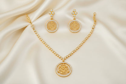 Gold-tone necklace and matching drop earrings set with circular Om symbols surrounded by small clear stones, displayed on a plain white background.