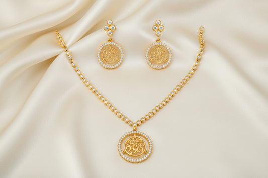 Gold-tone necklace and matching drop earrings set with circular Om symbols surrounded by small clear stones, displayed on a plain white background.